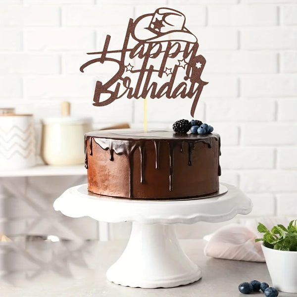 A dark chocolate birthday cake with a rustic western cowboy theme topper and blueberries on a white cake stand.