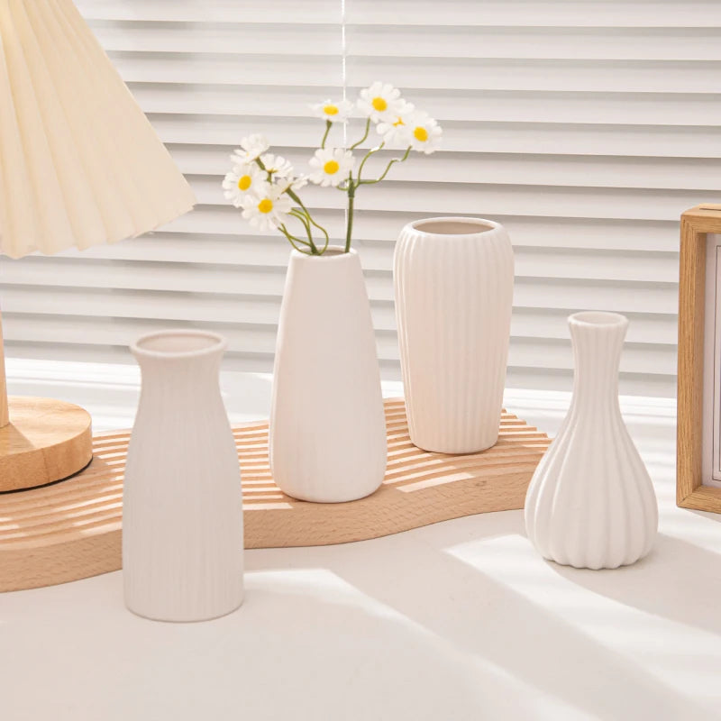 A collection of white ceramic bud vases and a plant arrangement displayed on a light wooden surface.