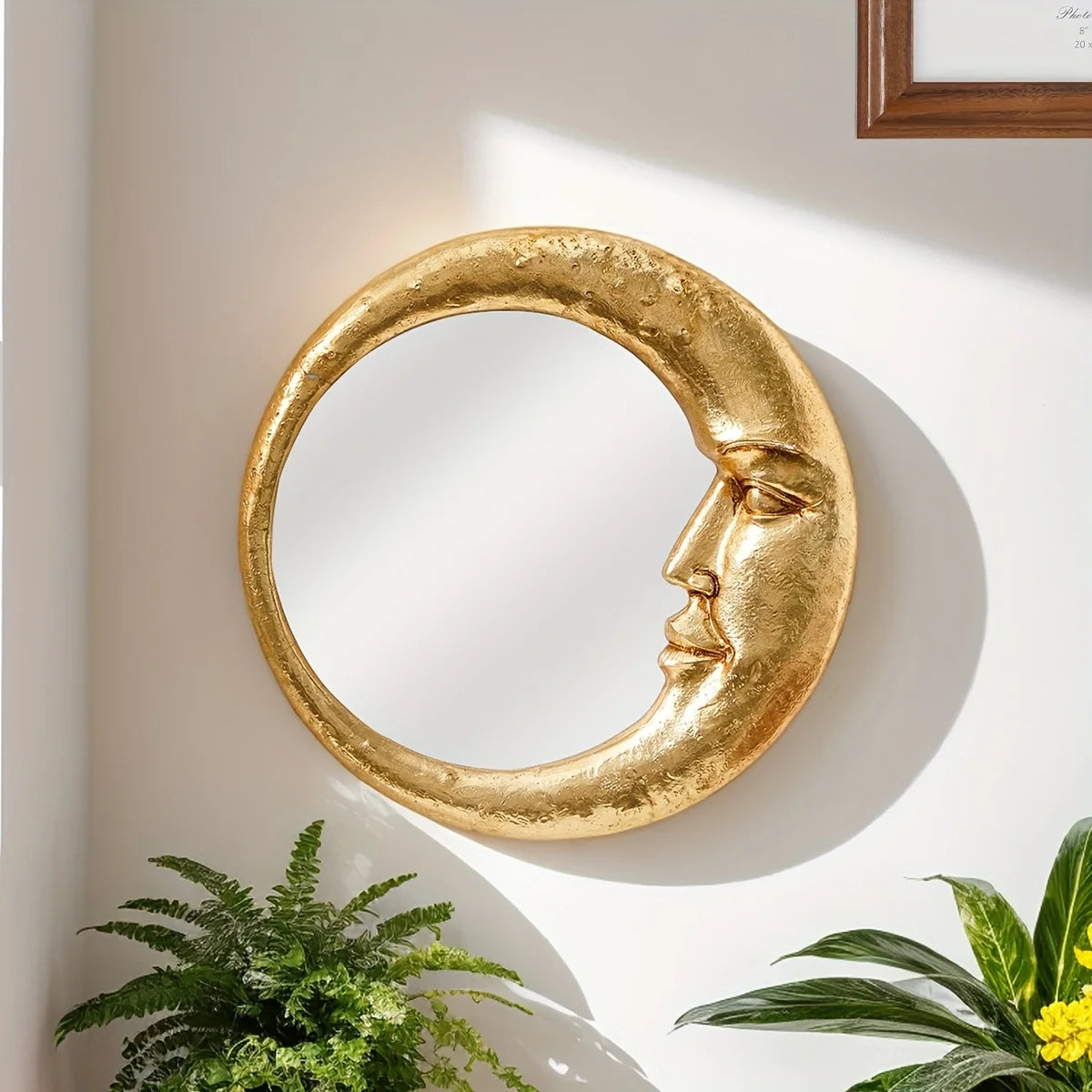 A round gold resin decorative hanging mirror with a stylized face is mounted on a white wall.