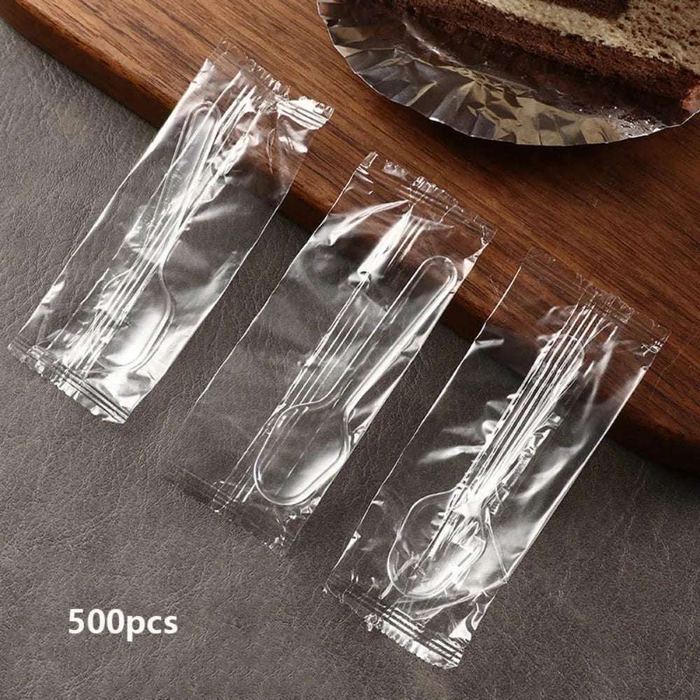 500 pieces of clear plastic disposable spoons packaged in a clear plastic pouch on a wooden board.