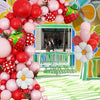 A vibrant balloon arch wreath featuring pink, red, and white balloons and strawberry accents in an outdoor setting.