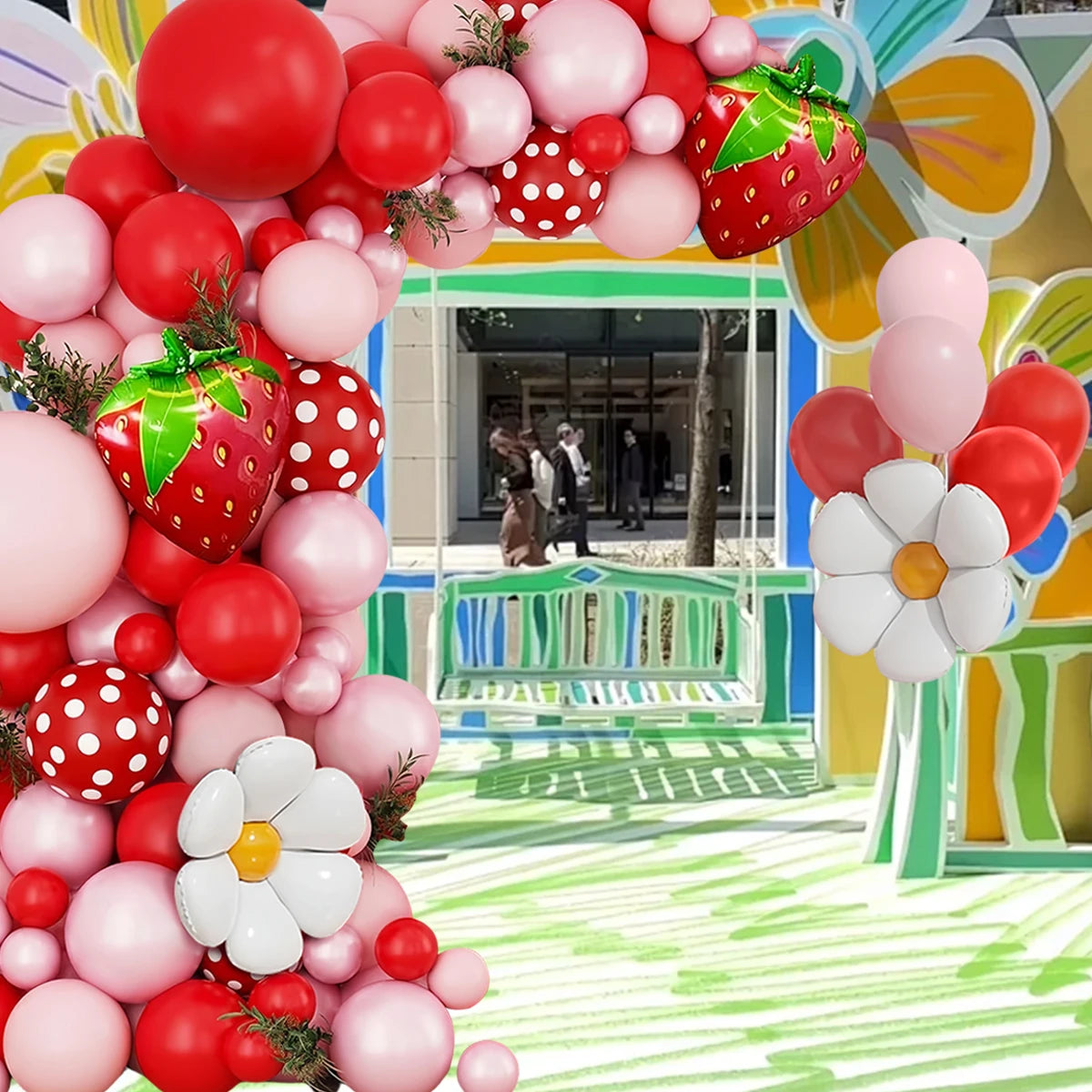 A vibrant balloon arch wreath featuring pink, red, and white balloons and strawberry accents in an outdoor setting.