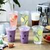 A collection of purple and green drinks in disposable plastic cups with lids, set on a wooden table next to an espresso machi