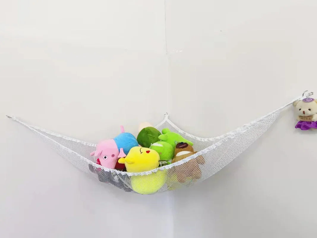 A mesh storage hammock holds various colorful stuffed animals and toys against a white wall.