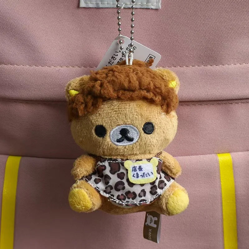 A brown Rilakkuma plush bear keychain hanging from a white tag against a pink fabric background.