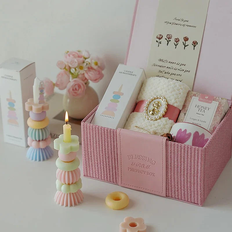 A pink gift box containing a candle, a small plant, and decorative items for aromatherapy.