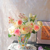 A bouquet of pink and cream roses and pink filler flowers in a ceramic bird floral vase on a dark table.