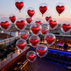 A display of red heart-shaped foil balloons and clear bubble balloons floating in the twilight setting of a bar or restaurant