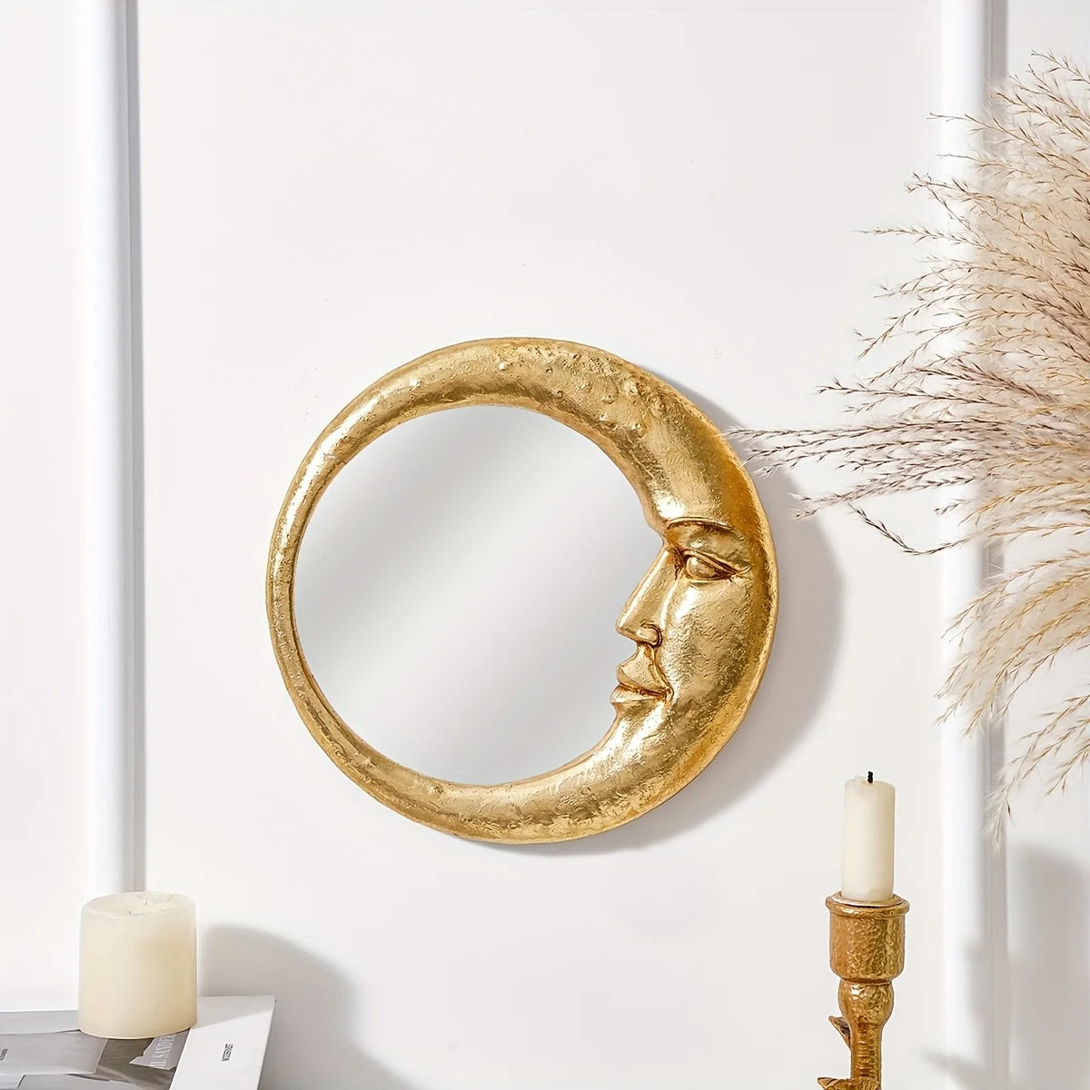 A round gold resin decorative hanging mirror is mounted on a white wall next to a lit candle.