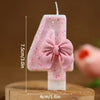 A pink glitter number cake candle set showing the number four with a bow on a wooden surface.