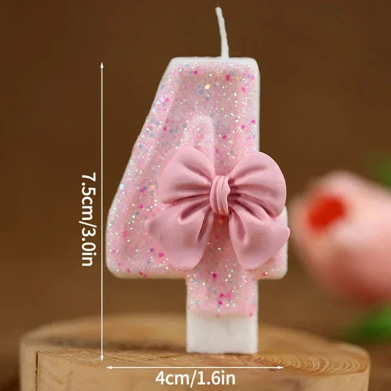 A pink glitter number cake candle set showing the number four with a bow on a wooden surface.