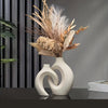A set of two white, organic-shaped vases holding dried grasses and foliage on a dark surface.