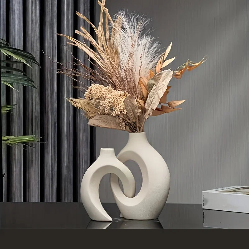 A set of two white, organic-shaped vases holding dried grasses and foliage on a dark surface.