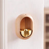 A wooden doorbell with a copper bell is mounted on a white door frame.