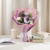 A pink handmade crochet rose flower bouquet with green leaves displayed on a white table.
