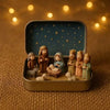 A hand-painted mini nativity set featuring figures and animals displayed in a gold tin storage box against a dark blue starry