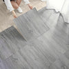 A close-up view of light gray wood grain self-adhesive decor stickers being applied to a wooden floor.