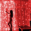 A woman stands in front of a bright red curtain decorated with glowing fairy lights.