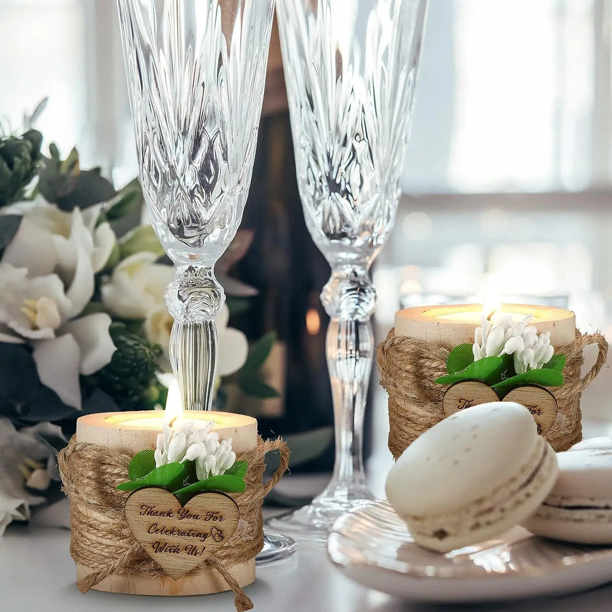 Clear glass trumpet candle holders with white flowers and macarons displayed on a table.