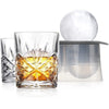 A clear whiskey glass filled with amber liquid sits next to a large, clear ice sphere and a gray storage container.