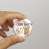 A hand holds a round pink pin badge featuring a cartoon bear and the text Our Party Team Girl