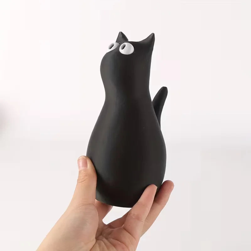 A black cat-shaped vase is held in a hand against a white background.