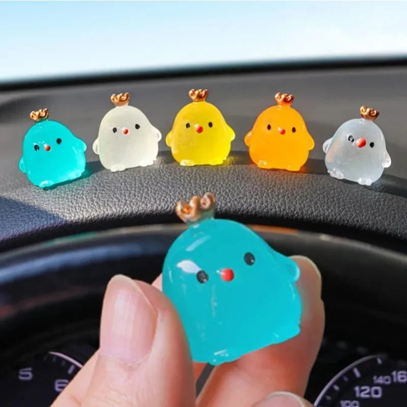 A hand holds a bright blue resin chicken car ornament next to several yellow and white chicken ornaments on a car dashboard.