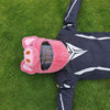A pink cartoon plush helmet cover lying on green grass next to a dark jacket.