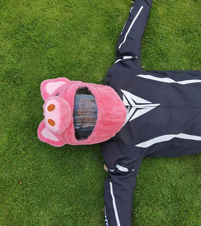A pink cartoon plush helmet cover lying on green grass next to a dark jacket.