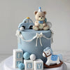 A light blue cake decorated with bear and car toppers, featuring baby blocks and a white horse design.