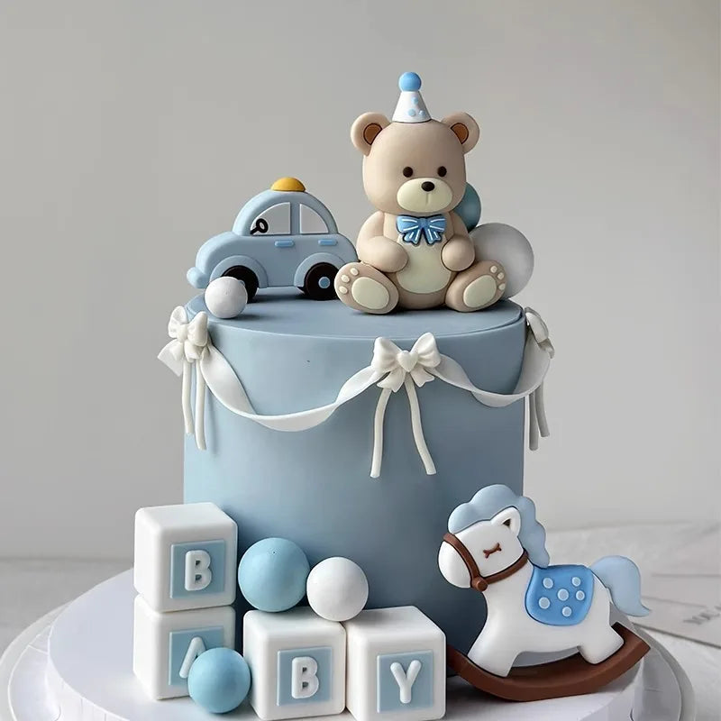 A light blue cake decorated with bear and car toppers, featuring baby blocks and a white horse design.