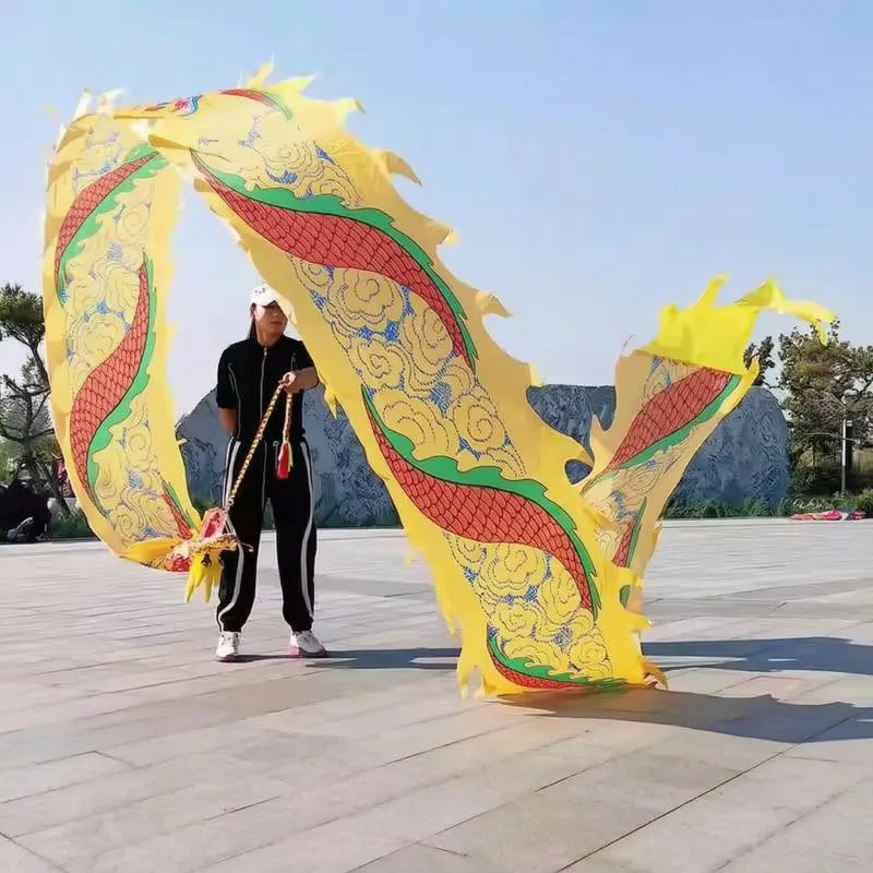 Una persona sostiene un gran utilería de danza de dragón amarilla con detalles rojos y verdes al aire libre.