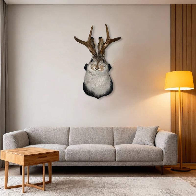 A decorative wall mount featuring a taxidermy bunny head with antlers mounted on a light gray sofa in a modern living room.