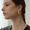 A close-up of a woman wearing gold-toned geometric stud earrings on her ear.