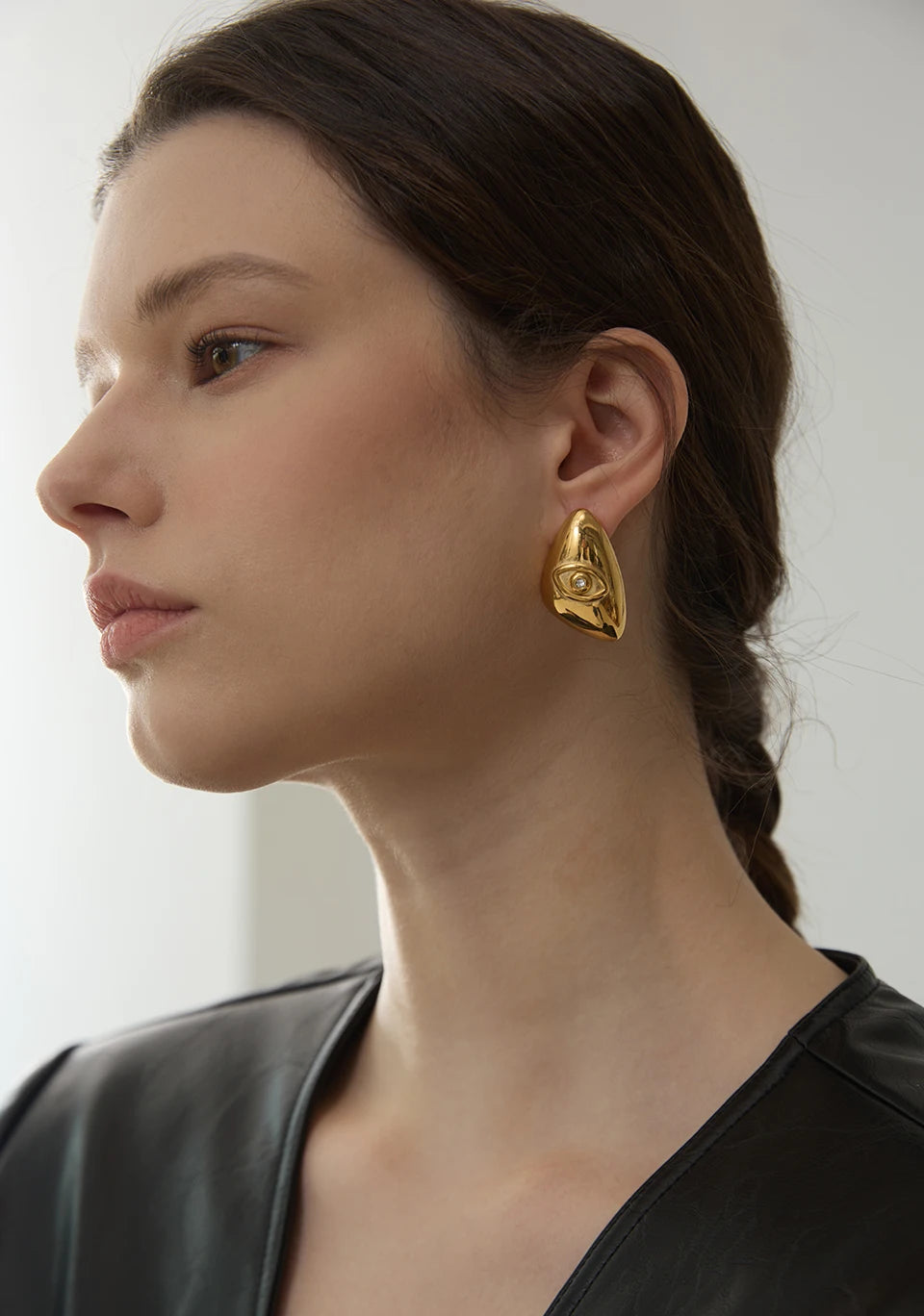 A close-up of a woman wearing gold-toned geometric stud earrings on her ear.
