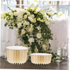 A floral centerpiece featuring white and yellow roses and greenery displayed on a folding dessert table stand.