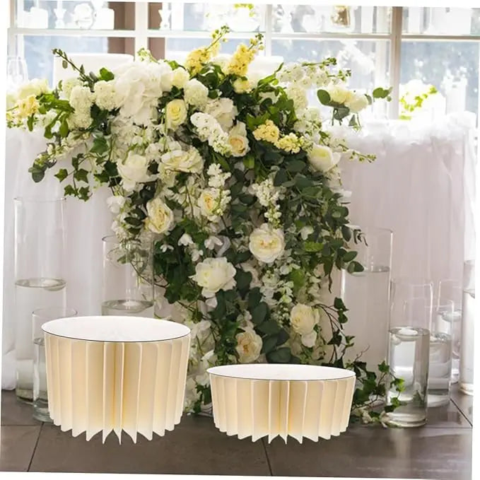 A floral centerpiece featuring white and yellow roses and greenery displayed on a folding dessert table stand.