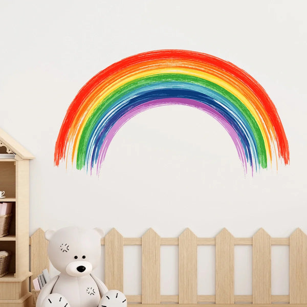 A vibrant watercolor rainbow arch decoration displayed on a white wall above a wooden fence.