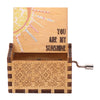 A vintage hand crank music box with a light wood box featuring a sun design and decorative carving.
