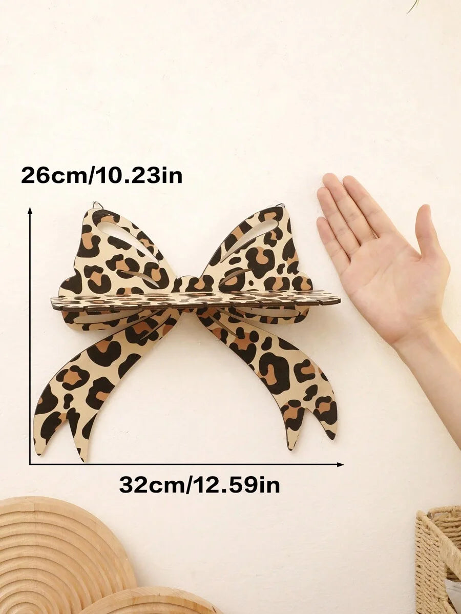 A leopard print bow-shaped wall mounted storage rack shown next to a hand for scale.