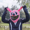A person wearing a pink cartoon plush helmet cover with rabbit ears and a black jacket, posing outdoors.