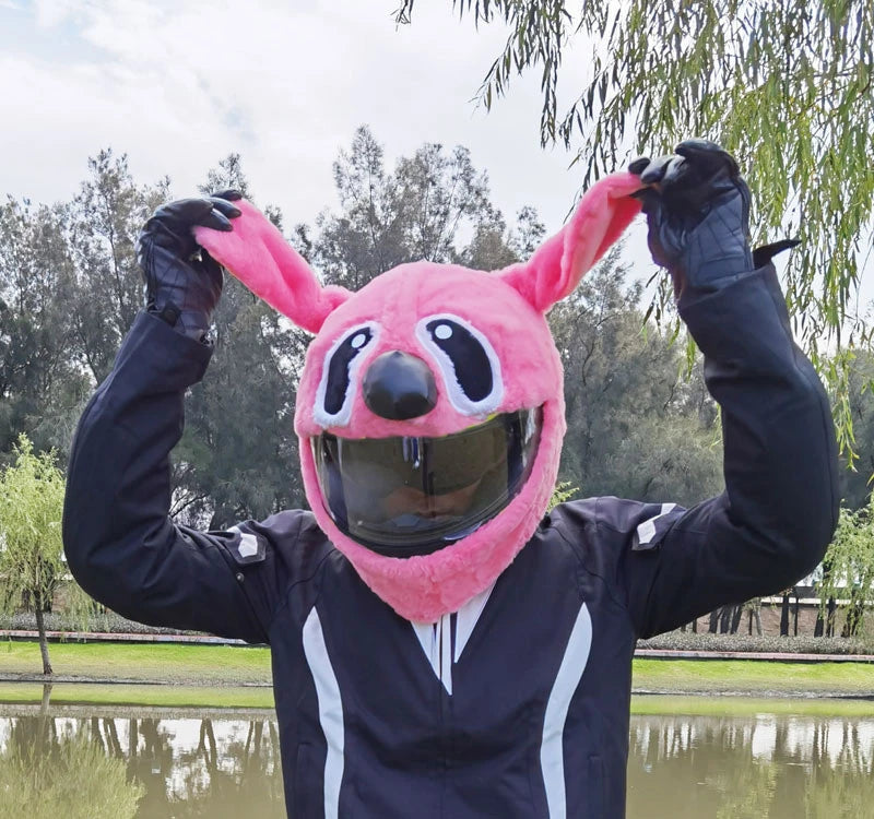 A person wearing a pink cartoon plush helmet cover with rabbit ears and a black jacket, posing outdoors.