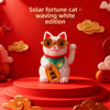 A white ceramic fortune cat ornament with gold-rimmed glasses and a green collar, displayed on a red circular stand.