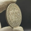 An antique silver-gray decision coin with a floral design is held by a hand.