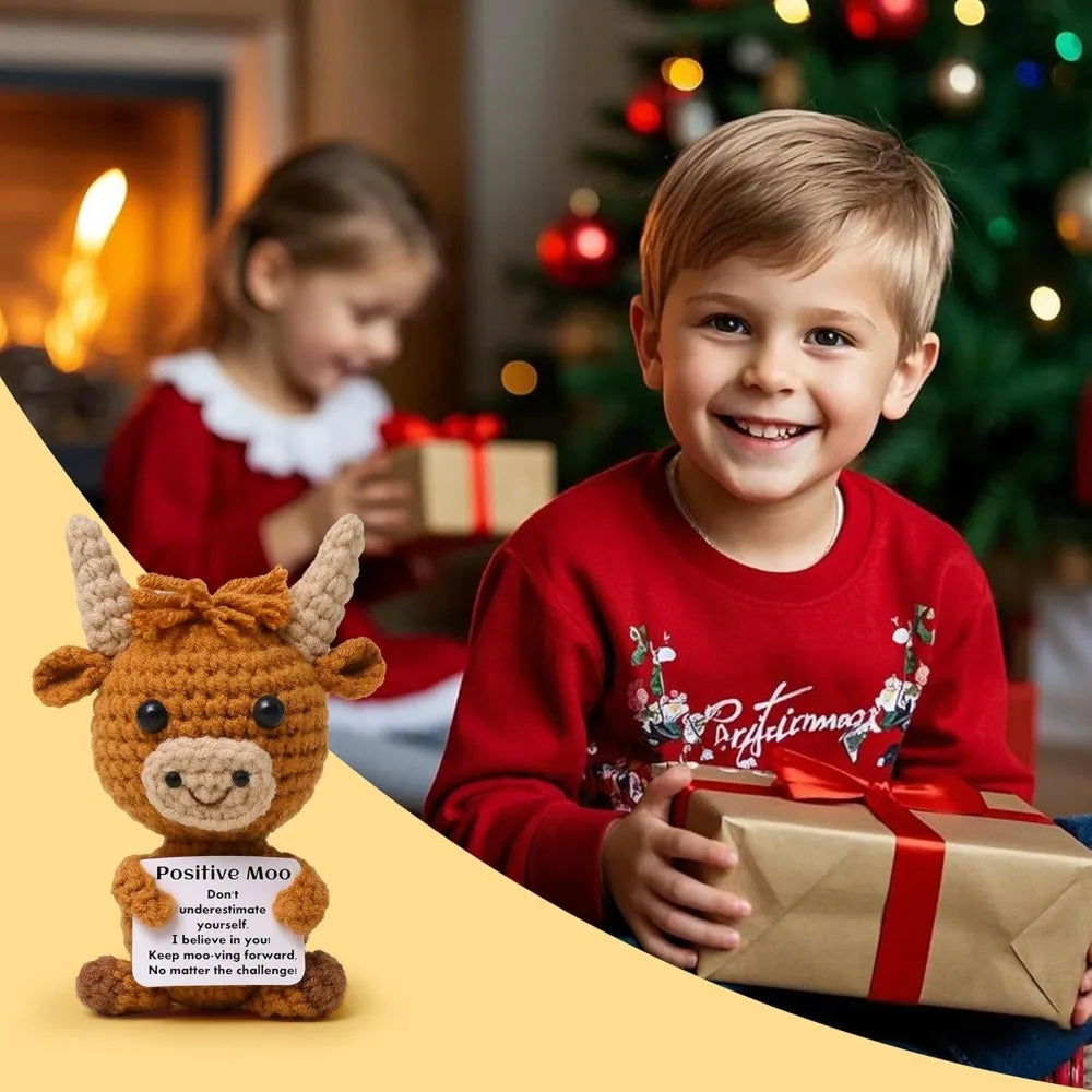 A smiling boy holds a wrapped gift while a crocheted Highland cow keychain sits beside him.
