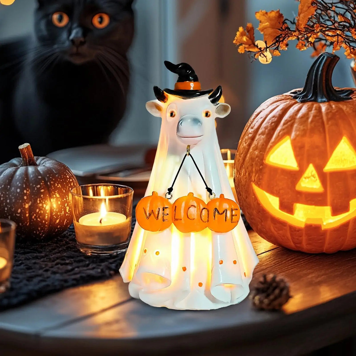 A white illuminated ghost figurine with horns and a witch hat sits next to a carved pumpkin on a wooden surface.