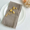 A handcrafted fringed cotton napkin resting on a white plate with dried yellow flowers.