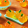 Bright orange mini artificial pumpkins are displayed on a wooden surface and in a light blue basket.
