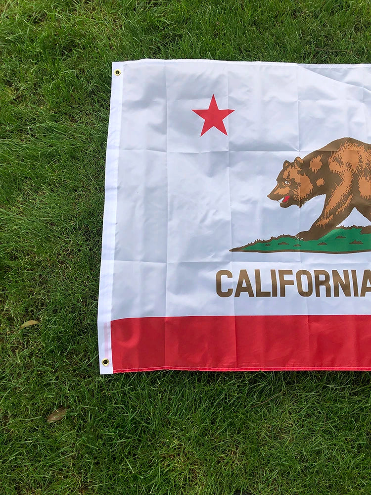 A white flag featuring a red star and a brown bear silhouette on the left, with the word CALIFORNIA in gold text across the b