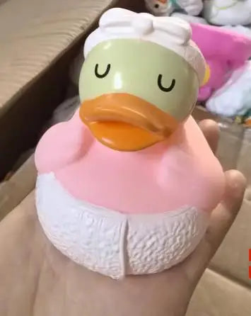 A cute rubber duck bath toy with a yellow beak and pink body is held in a hand.